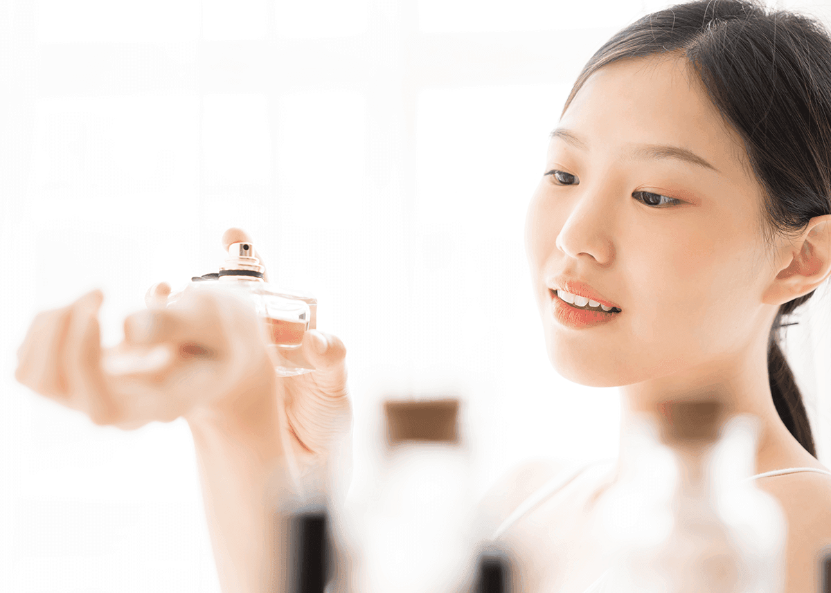 bright asian woman applying perfume to wrist