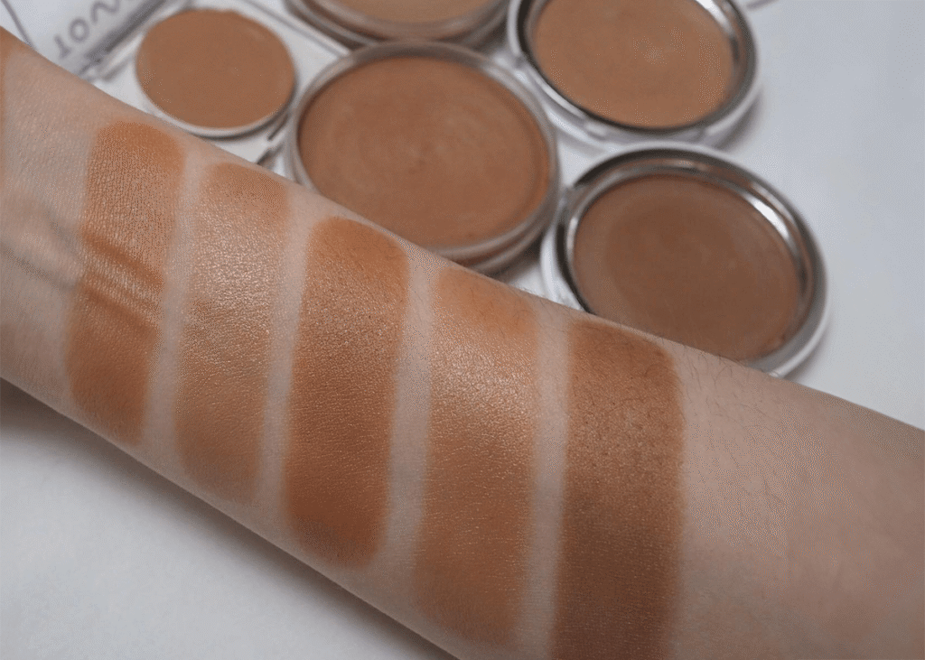A woman with different skin tones swatching shades of bronzer on her arm